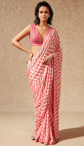 Elegant pink georgette saree adorned with a stylish chevron print and delicate sequin embroidery. paired with a sleeveless silk blouse featuring v-neck and tassel tie-up detailing for a sophisticated look.