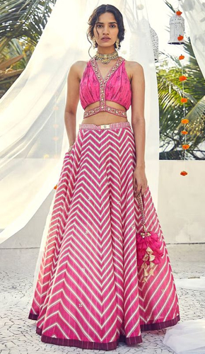 Captivating pink chevron-print lehenga adorned with sequin highlights, paired with a sleeveless floral-embroidered blouse and an elegant v-neckline – a perfect ensemble for a touch of grace and glamour.